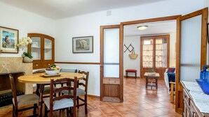 Zona pranzo con un tavolo rotondo, sedie, un camino e una cucina visibile attraverso un'apertura.