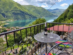 A balcony with a table and chairs, overlooking a lake and mountains.