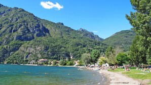 A beach with clear water, a sandy shore, and a backdrop of green mountains. - Casa Pina by Interhome (Porlezza)