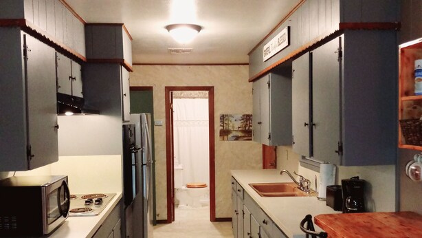 A narrow kitchen with a central island, a microwave, a stove, and a sink.