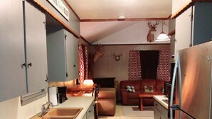A compact kitchen with a sink, stove, and refrigerator. There is a dining table and a couch in the adjacent living area.