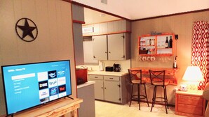 A compact living space with a TV on a wooden stand, a kitchenette with a microwave, and a bar area with stools.
