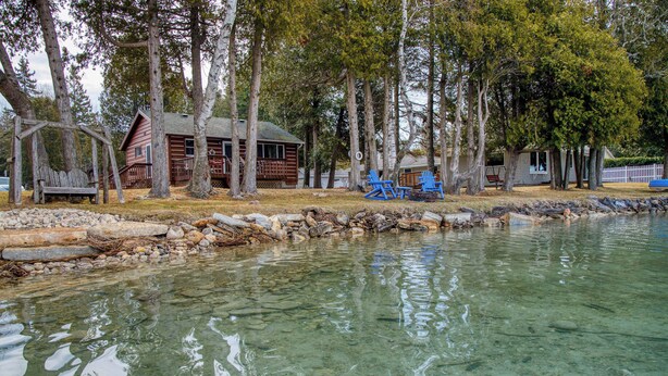 Een chalet aan een helder meer, met een houten terras en een klein steigertje.