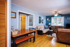 A living room with a wooden floor, a sofa, a table with a bench, and a ceiling fan.