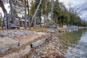 A lakeside cabin with a dock, surrounded by trees and a rocky shoreline.