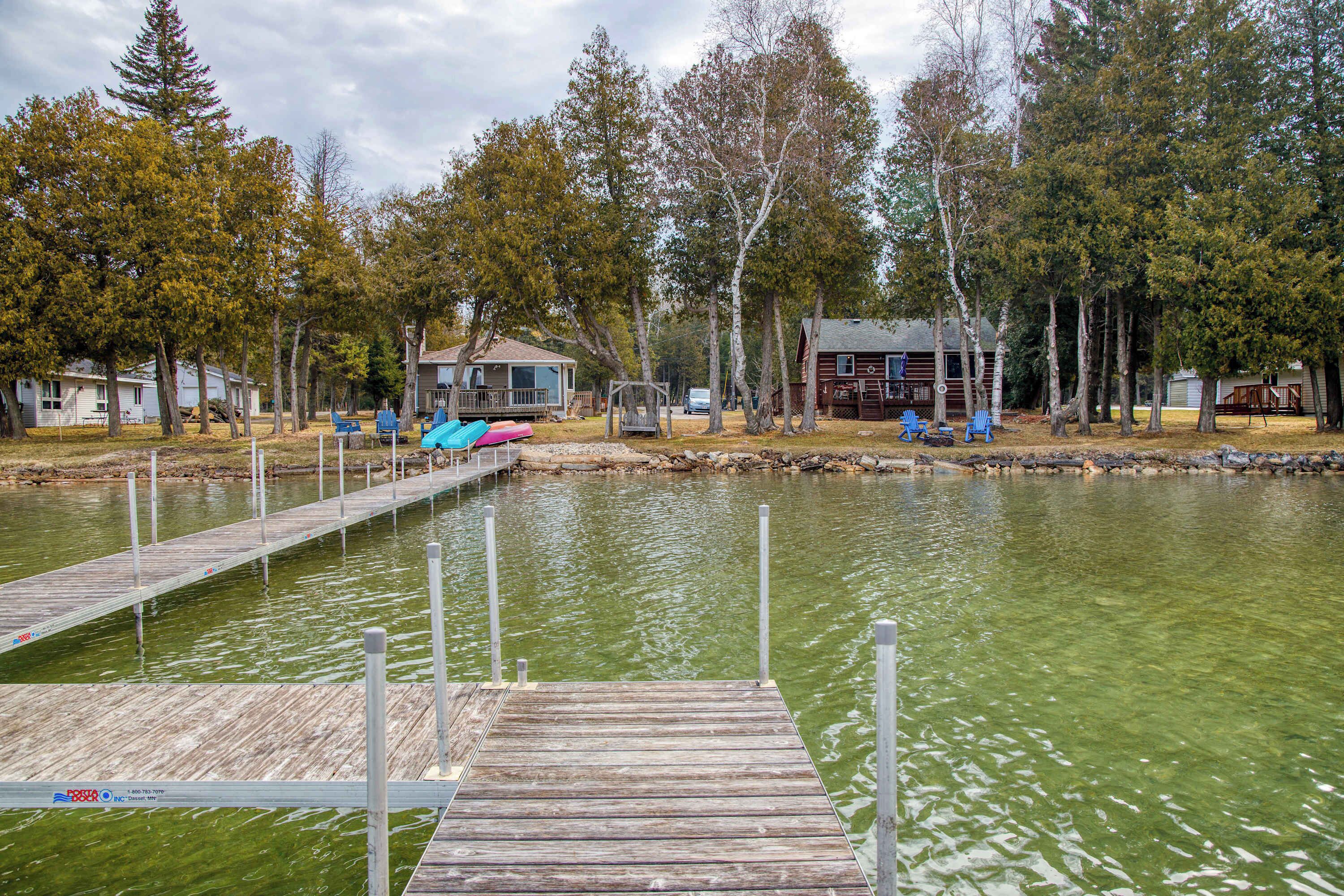 Um cais de madeira que se estende por um lago, com uma fileira de cabanas e um pequeno edifício ao fundo.