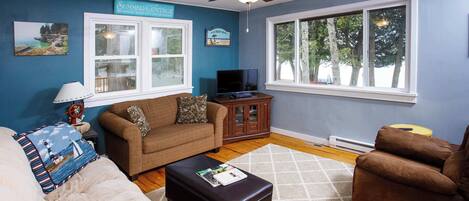 A living room with a ceiling fan, a television, a sofa, a coffee table, and a window with a view of trees.