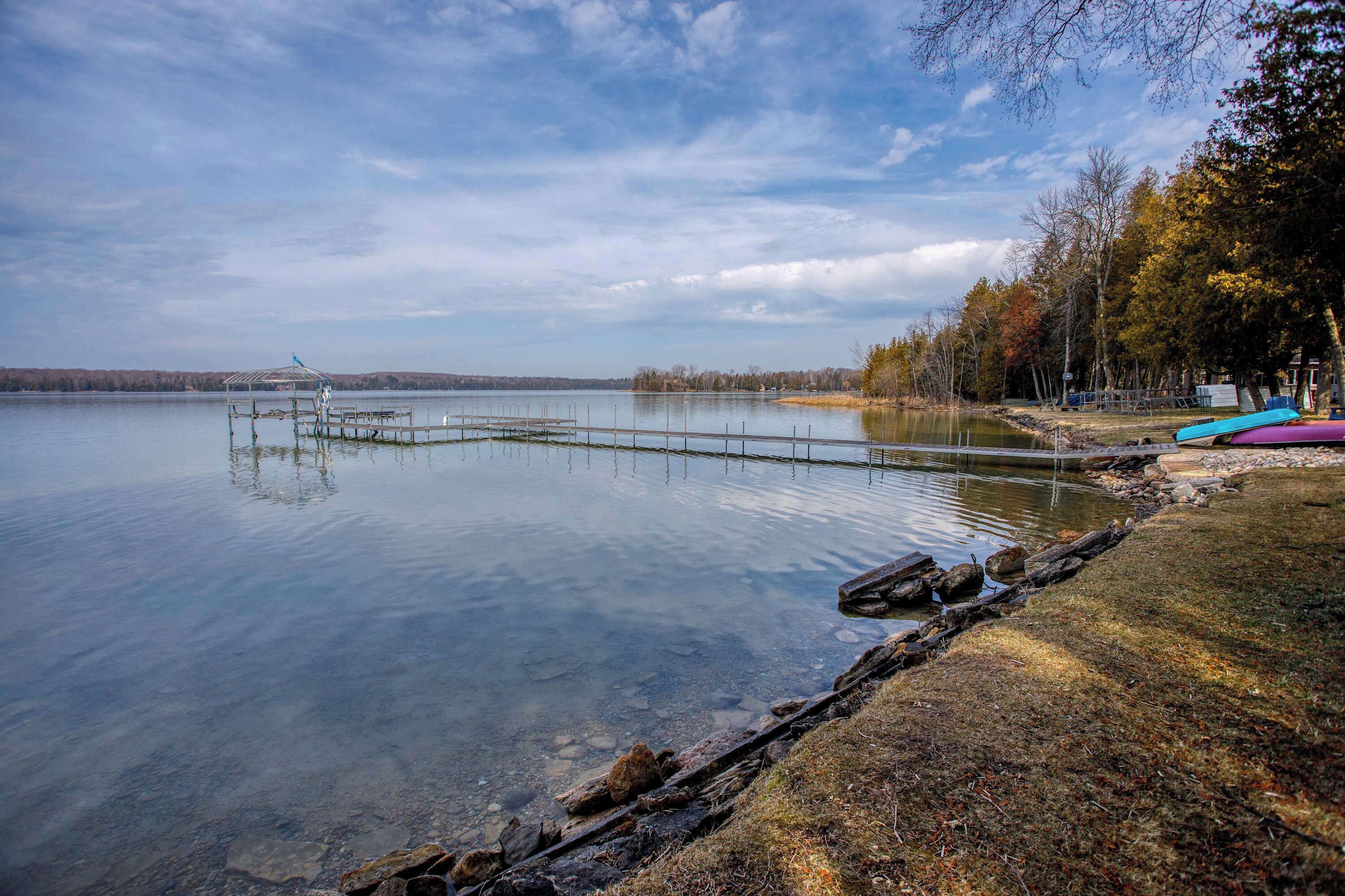 Um lago calmo com um píer que se estende na água, cercado por árvores e um céu claro.