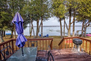 A deck with a grill, chairs, and an umbrella overlooking a lake.