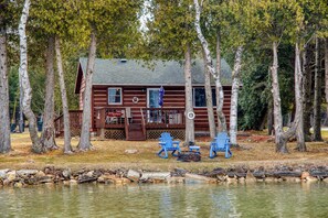 A cabin with a dock, surrounded by trees, and two blue chairs on the dock.