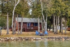 A cabin with a dock, surrounded by trees, and a small dock area with chairs.
