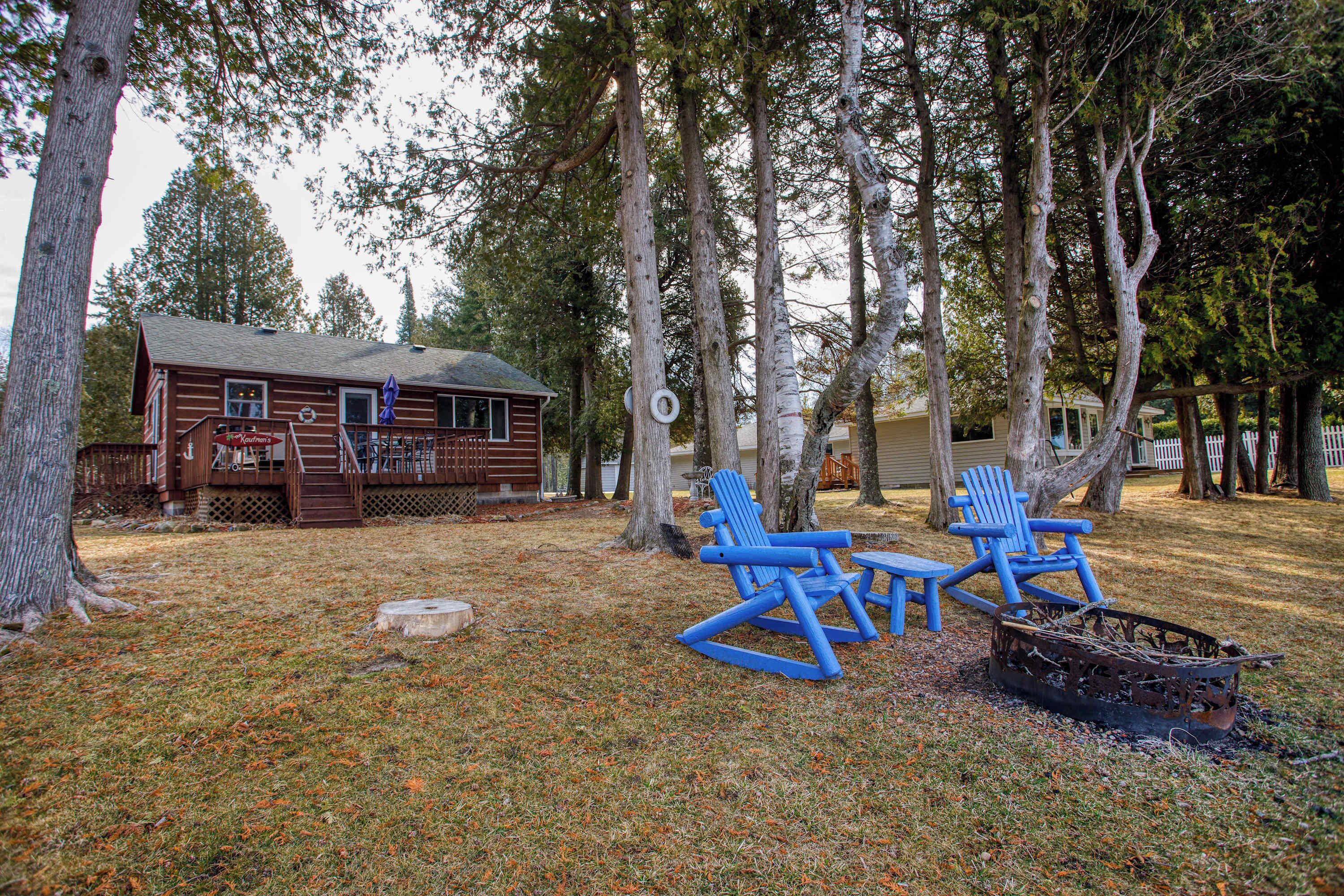 A cabin with a deck, a fire pit, and blue Adirondack chairs.