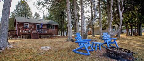 A cabin with a deck, a fire pit, and blue Adirondack chairs.