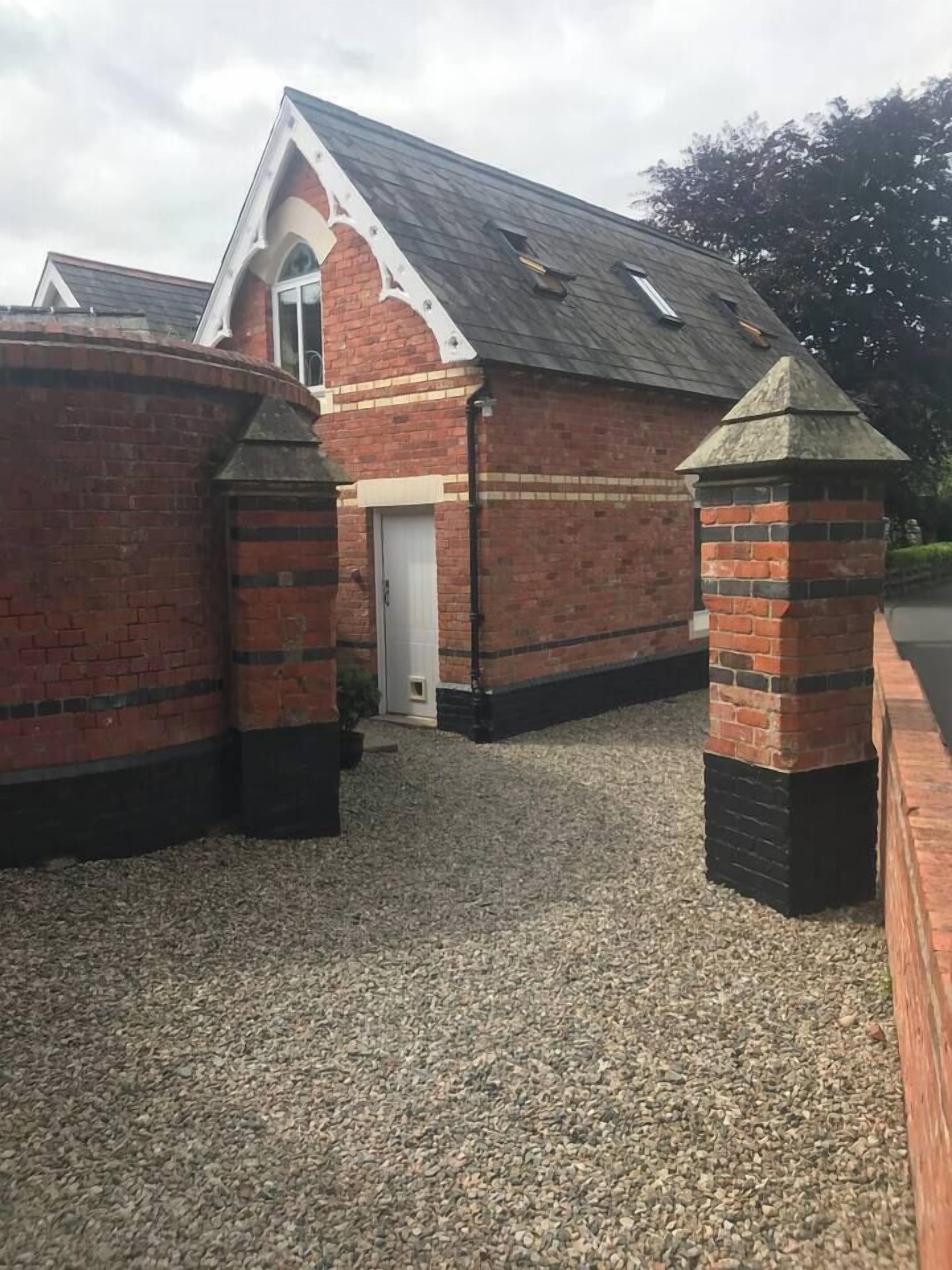 A brick building with a white door, a small window, and a gravel driveway.