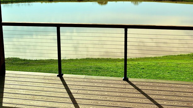 Une terrasse en bois avec une balustrade donnant sur une étendue d’eau calme et un paysage verdoyant.