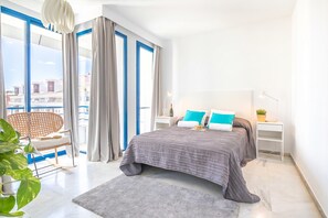 A modern bedroom with a large bed, a chair, a nightstand, and a view of buildings through large windows. - Marbella pool House PH77 on sea shore, Marbella, Spain (Marbella)