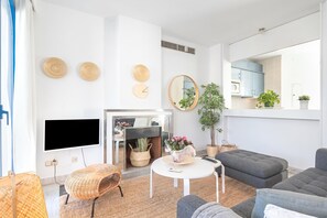 Un salon moderne avec un téléviseur à écran plat, des meubles en osier, une table basse ronde et un canapé gris.