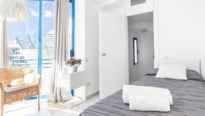 Habitación de hotel con una cama, una silla de mimbre, una mesita con un florero y vistas al exterior.