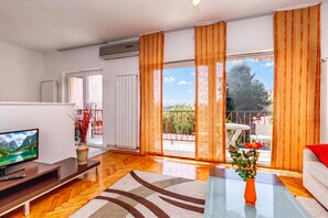 A modern living room with a flat-screen TV, a sofa, a coffee table, and a view of a balcony with outdoor furniture.