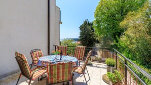 Eine Terrasse im Freien mit einem runden Tisch und gestreiften Stühlen, umgeben von viel Grün und freiem Blick zum Himmel.