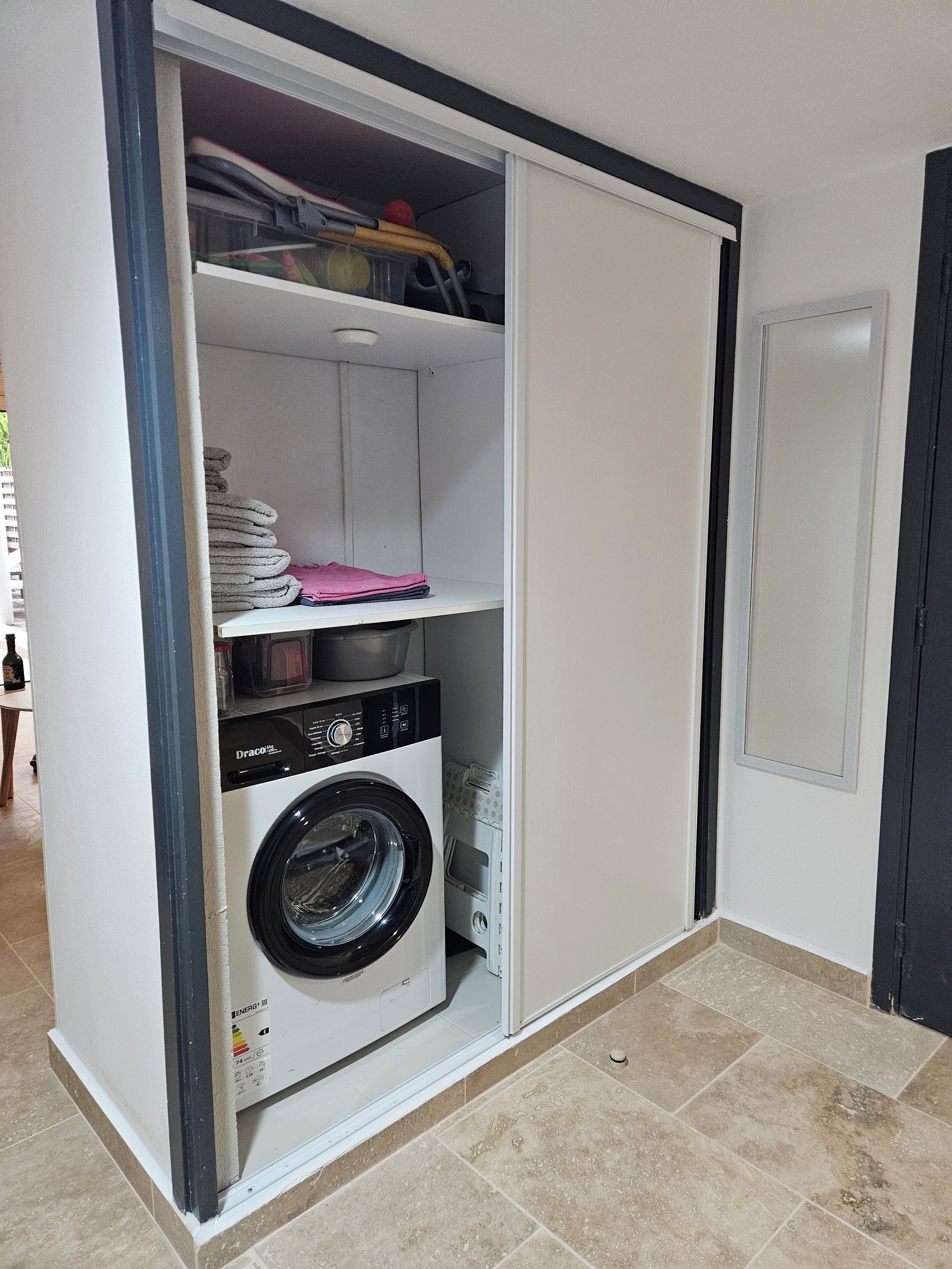 Une petite buanderie équipée d’un lave-linge, d’un sèche-linge et d’étagères pour le rangement.