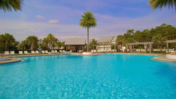 A large outdoor swimming pool surrounded by lounge chairs and palm trees, with a covered seating area in the background. - Bella Bonita by AvantStay | Pool, Peloton & Bikes, Golf Cart (Santa Rosa Beach)