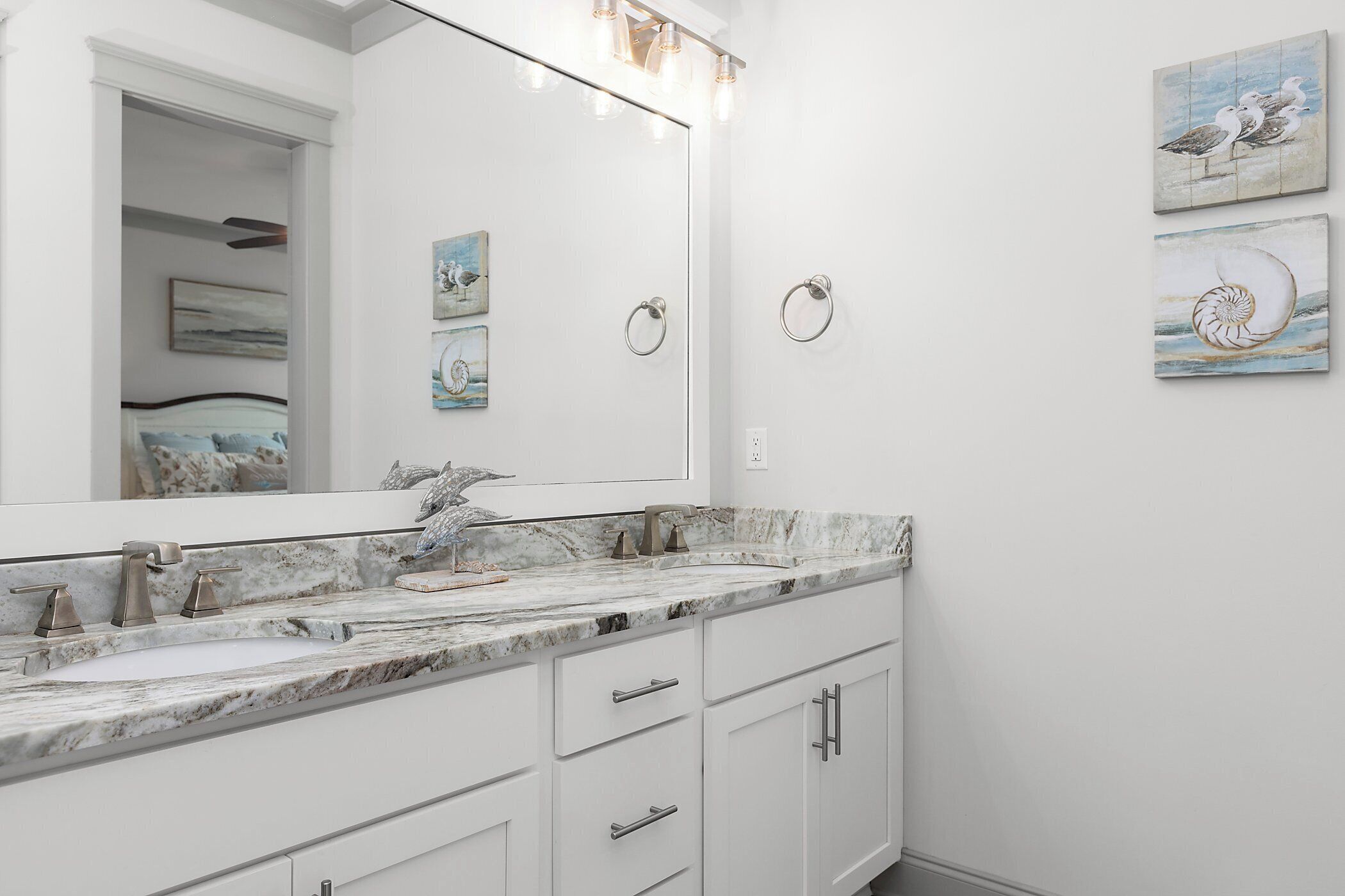 A bathroom with a white vanity, a large mirror, and artwork on the wall.
