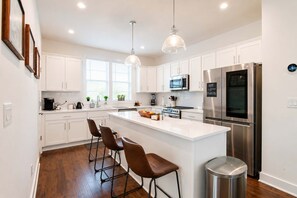 A modern kitchen with white cabinetry, stainless steel appliances, and a central island with bar stools. - Rooftop Creative Oasis – Close to Broadway (Nashville)