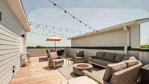 An outdoor deck with a wooden floor, wicker furniture, a round table, and string lights.