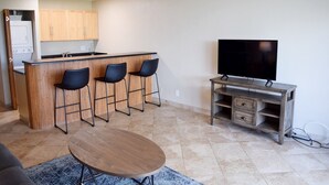 Un espace de vie compact comprenant un coin cuisine, un espace repas avec une table ronde et un téléviseur posé sur un meuble en bois.