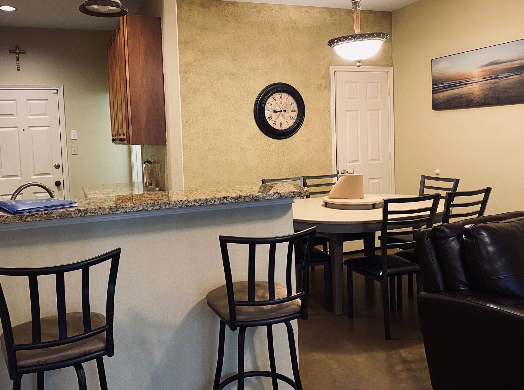 A dining area with a round table, chairs, a clock, and a painting on the wall.