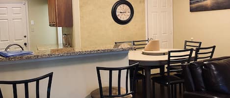 A dining area with a round table, chairs, a clock, and a painting on the wall.
