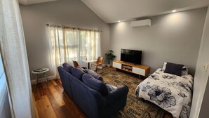 A modern living room with a sofa, a TV, a small table, and a bed with a floral bedspread. - Farm stay Guesthouse (Gnarwarre)