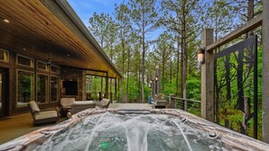Un jacuzzi con cubierta de madera, rodeado de árboles y un muro de piedra.