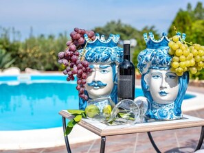 Two ceramic statues with grapes and a bottle on a table by a pool. - La Vela by Interhome (Scopello)