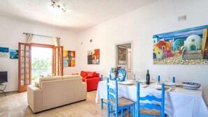 Un comedor con una mesa blanca dispuesta para cuatro, sillas azules y un cuadro de edificios coloridos en la pared.