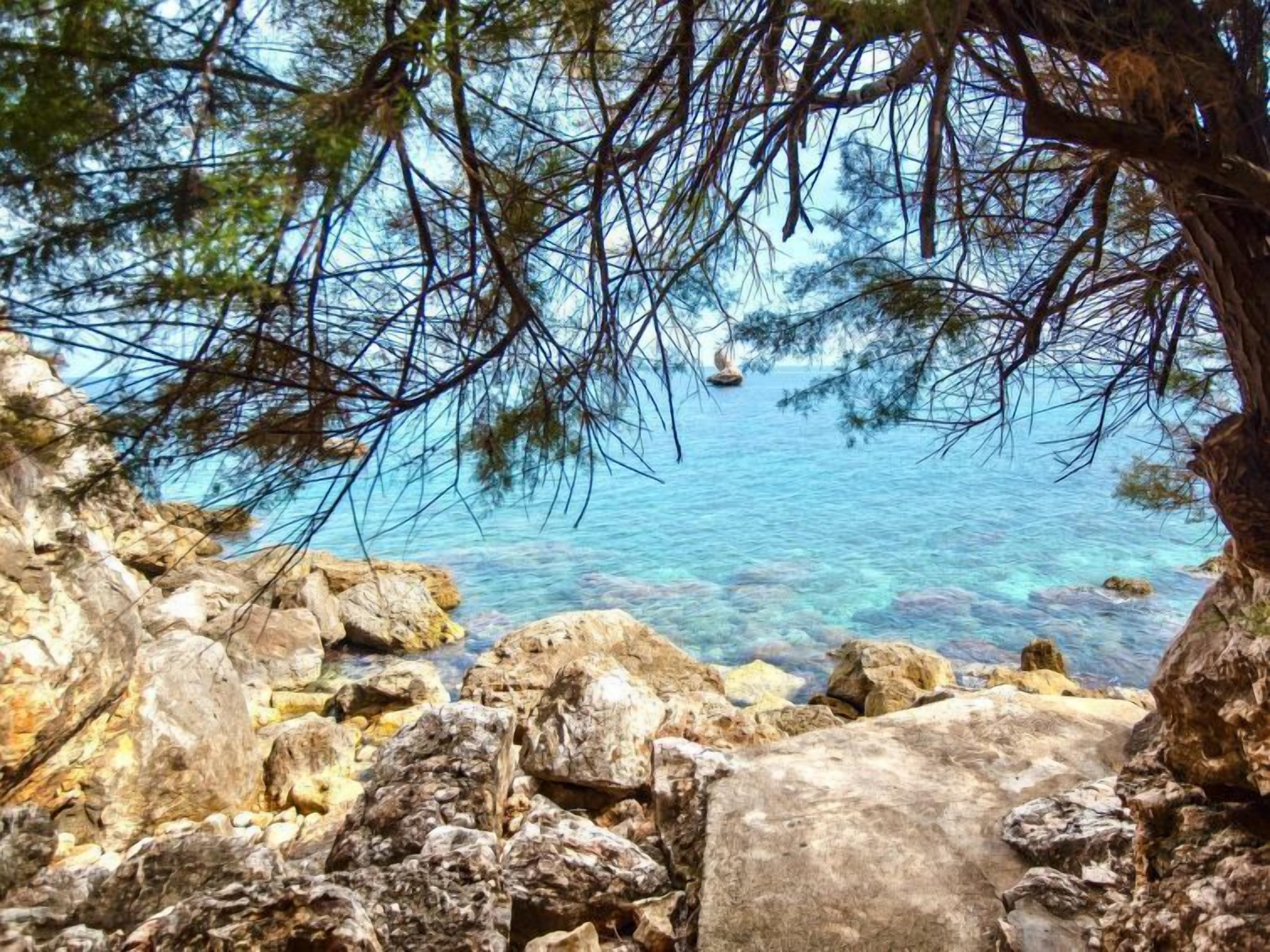 Eine felsige Küstenlinie mit klarem, blauem Wasser und einem Segelboot in der Ferne.