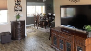 Een ruime woonkamer met een grote flatscreen-tv, houten meubels, een plafondventilator en een decoratief kunstwerk.