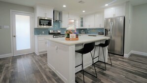 A modern kitchen with white cabinets, a stainless steel refrigerator, a microwave, and a coffee bar.