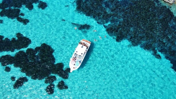 A boat on clear turquoise water with dark underwater rocks. - Egadi Islands Boat Excursions (Trapani)