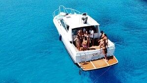 A white boat with a deck area where people are standing and sitting. - Egadi Islands Boat Excursions (Trapani)