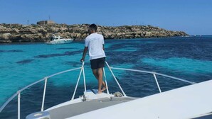 A person standing on a boat's deck, overlooking a rocky coastline with clear blue waters. - Egadi Islands Boat Excursions (Trapani)