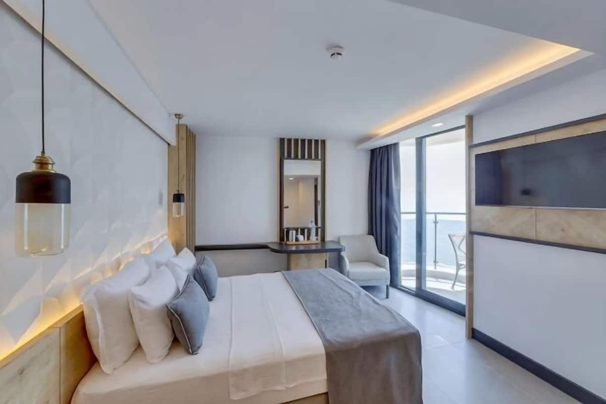 Ein modernes Hotelzimmer mit einem großen Bett, einem Schreibtisch, einem Sessel und einem großen Fenster mit Blick.