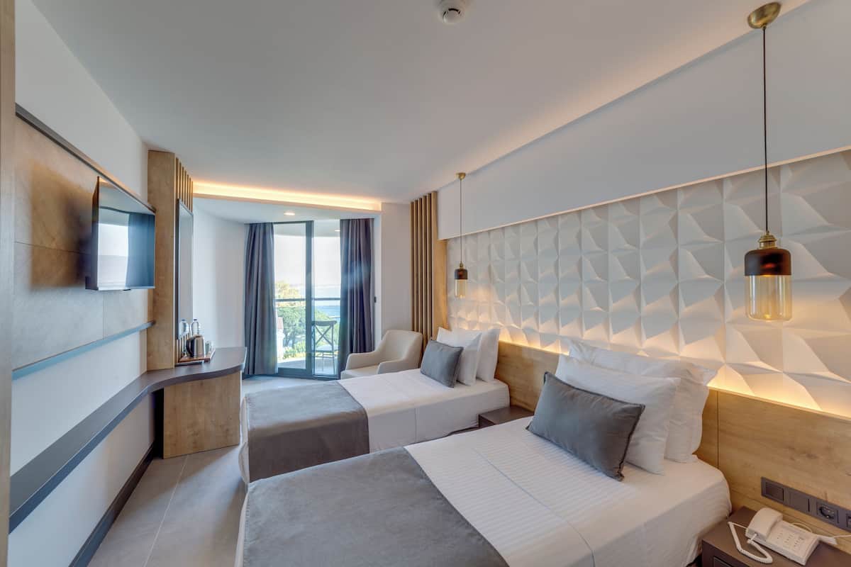 Ein Hotelzimmer mit zwei Betten, einem Fernseher, einem Schreibtisch und Blick ins Freie.