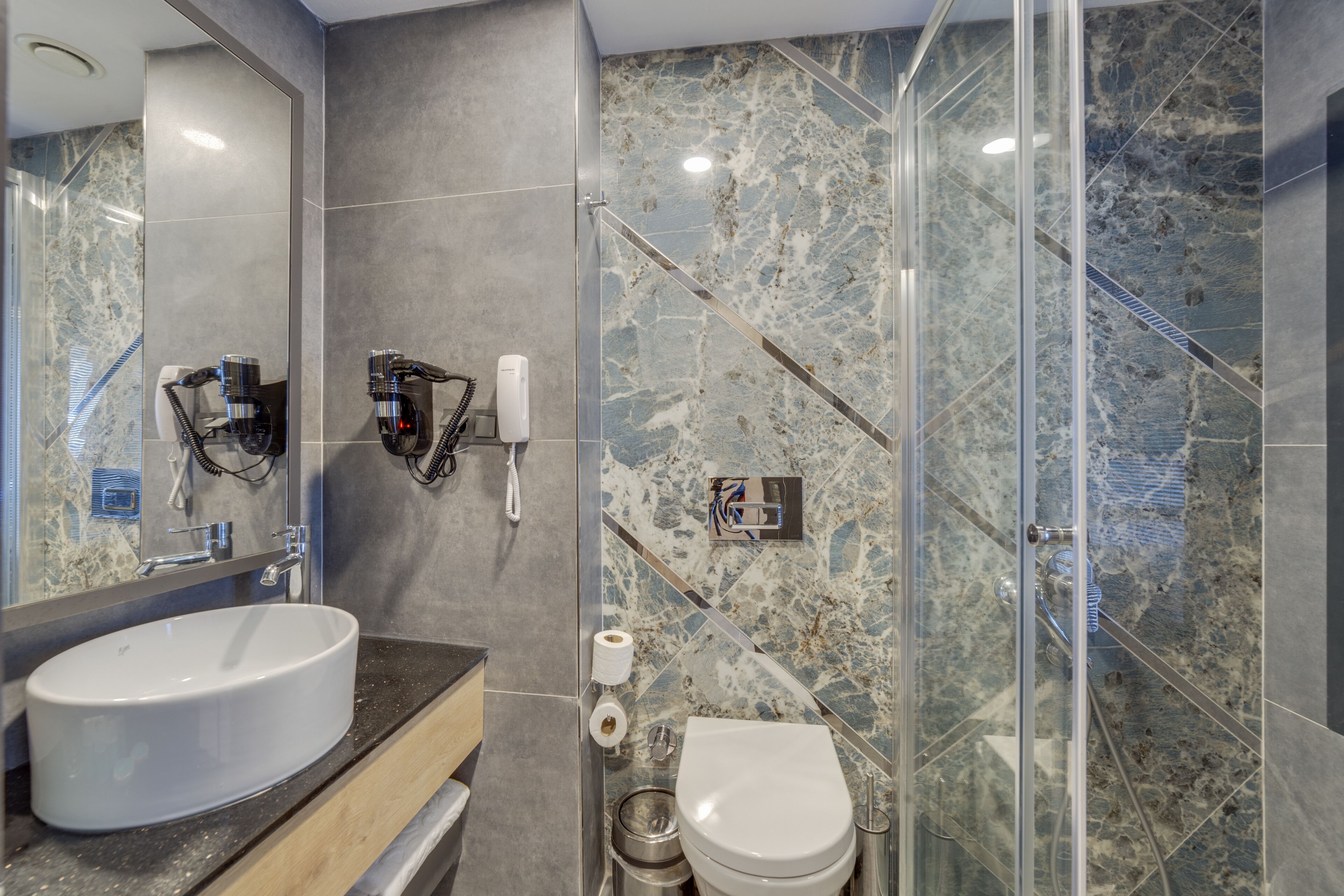 Un baño moderno con un lavamanos ovalado grande, un inodoro y un box de ducha de vidrio.