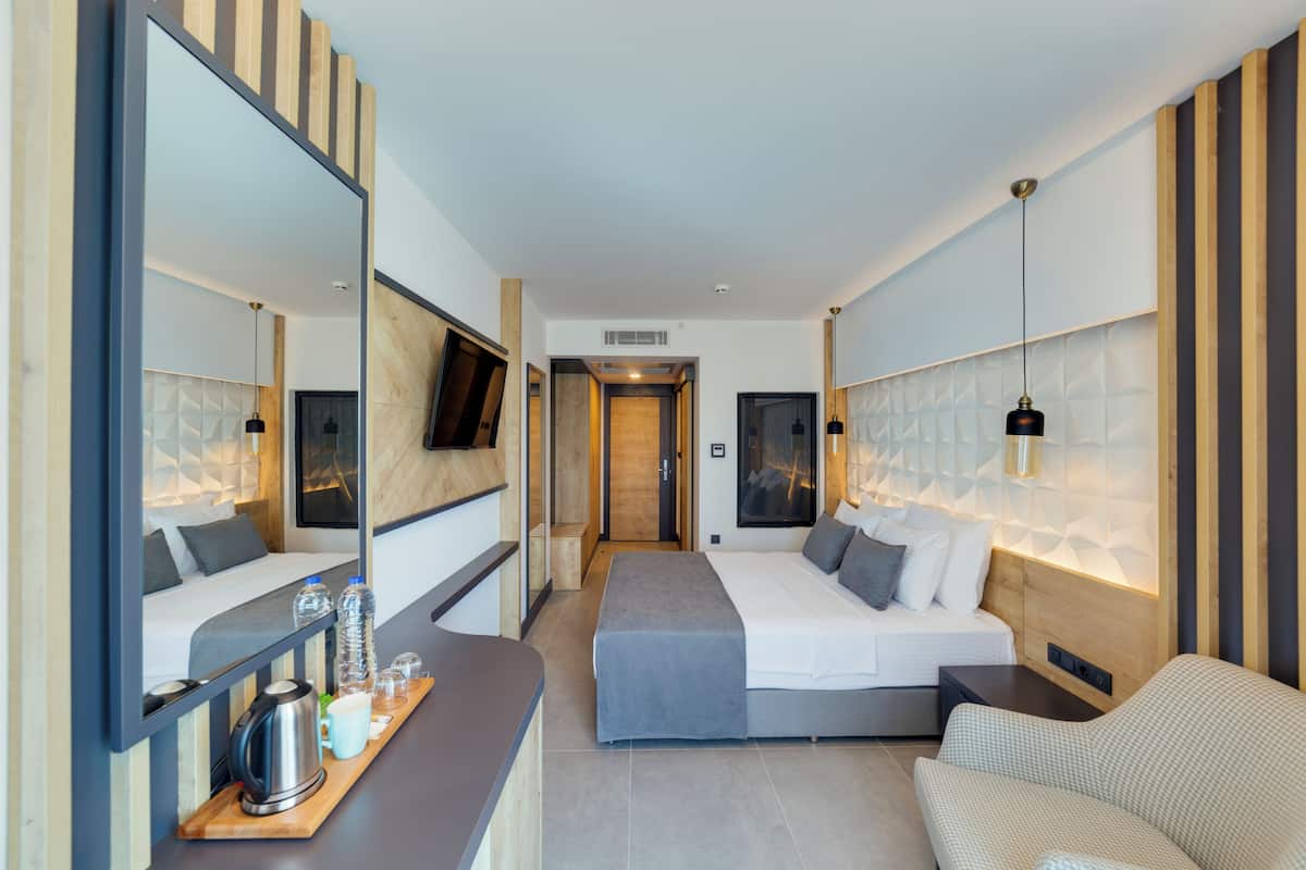 Ein modernes Hotelzimmer mit einem großen Bett, einer Sitzecke, einem Schreibtisch mit Wasserkocher und einem Spiegel.