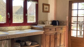 A kitchen with a tiled backsplash, wooden cabinets, and a window overlooking a stone building.