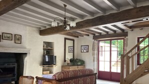 A rustic living room with exposed wooden beams, a fireplace, a television, a sofa, and a staircase.
