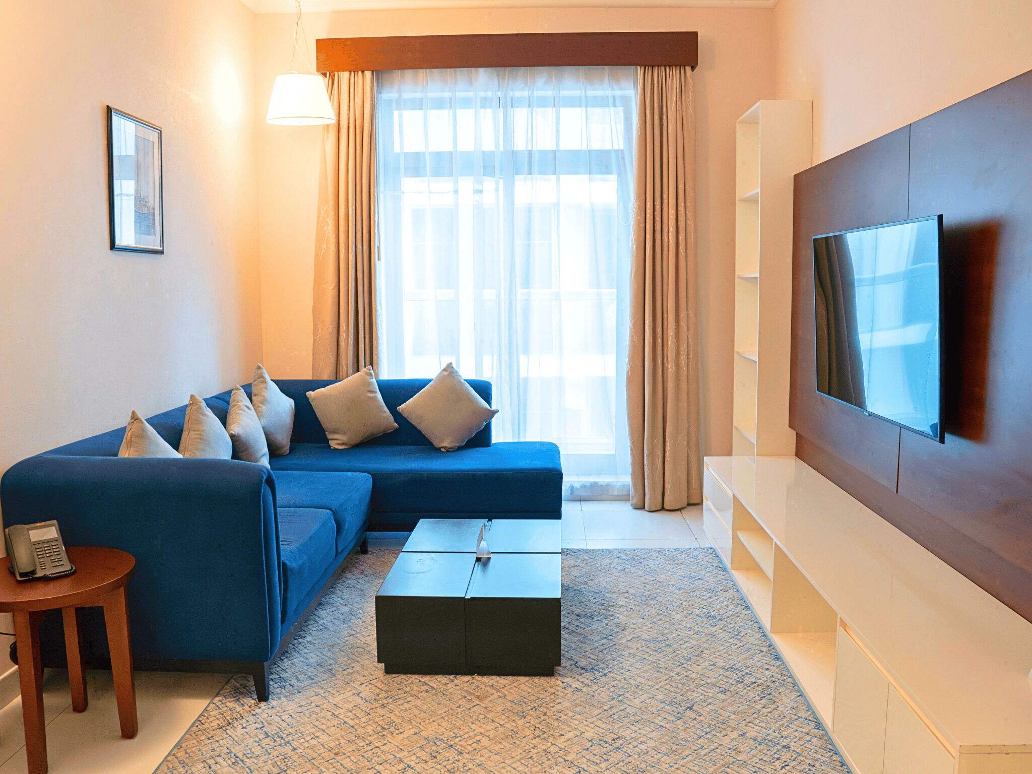 A living room with a blue sofa, a coffee table, a TV, and a small table with a phone.