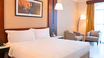 A hotel room with a large bed, a desk with a phone, a chair, a lamp, and a painting on the wall.